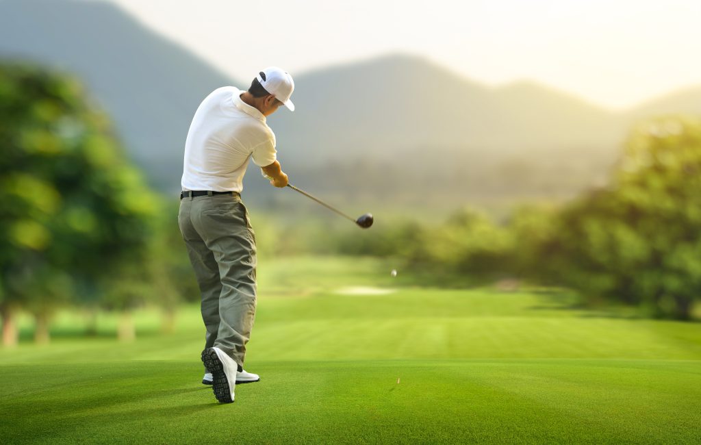 Golfer hitting golf ball with driver to fairway.